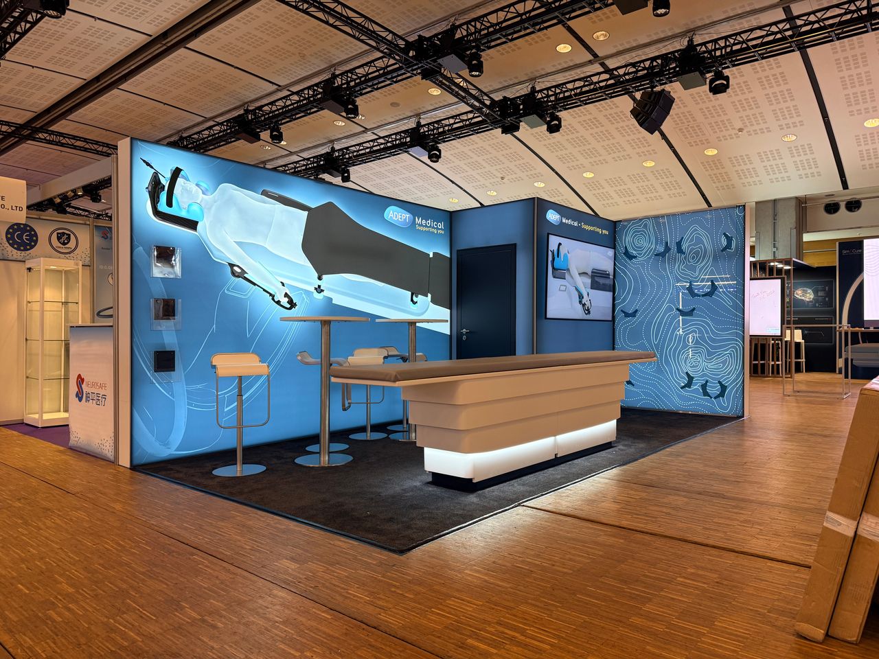 Adept Medical exhibition stand at LINNC in Paris: blue backlit graphic walls, long counter with illuminated base and bar tables