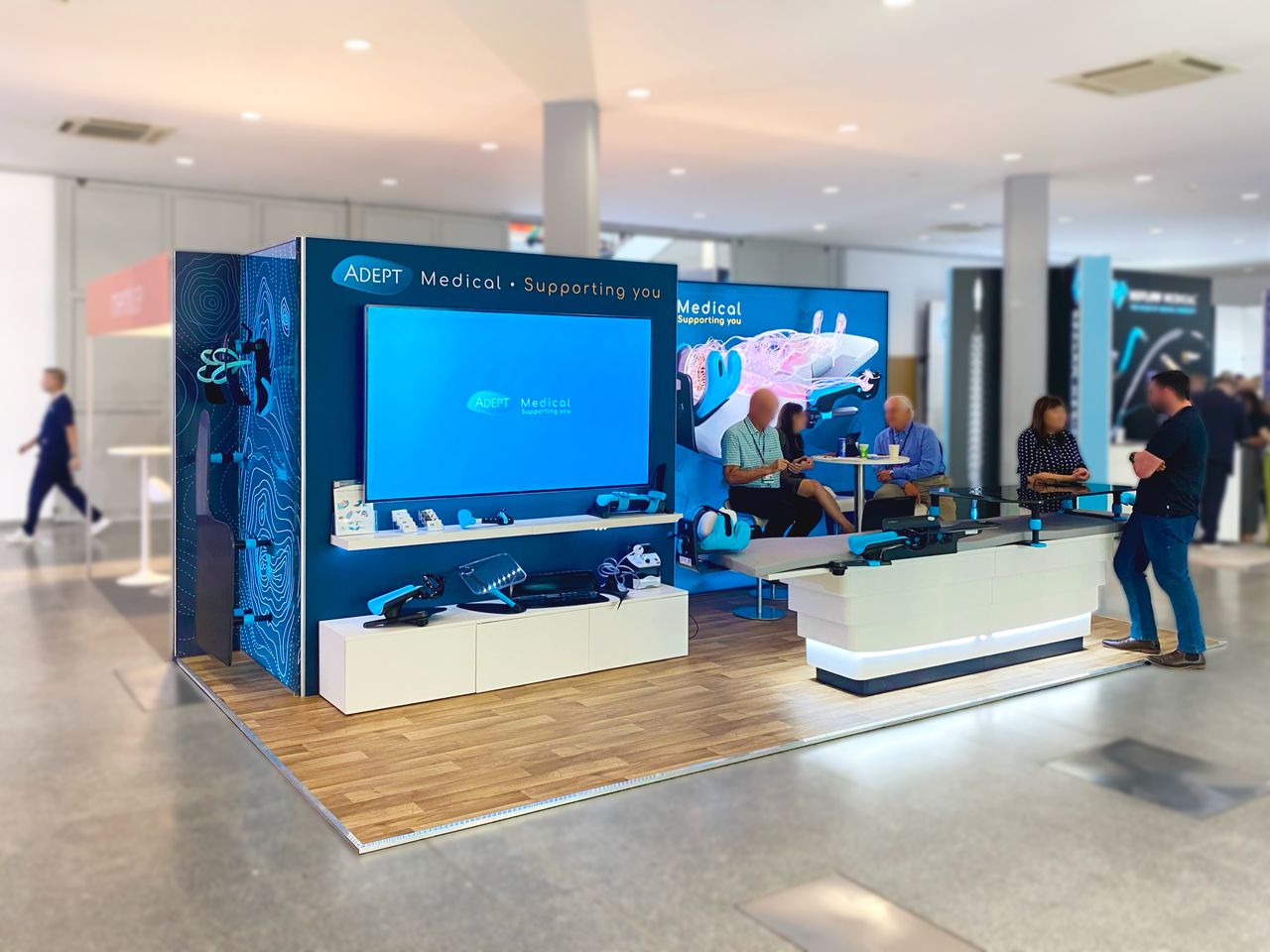 Adept Medical exhibition stand during the show: visitors talking at the counter and a bar table, product wall with a large screen