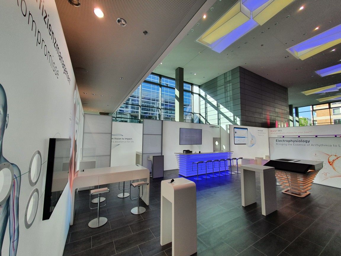 Bright Biotronik exhibition stand at the DGK annual meeting in Mannheim with a blue-lit slatted counter, bar tables and large graphic walls